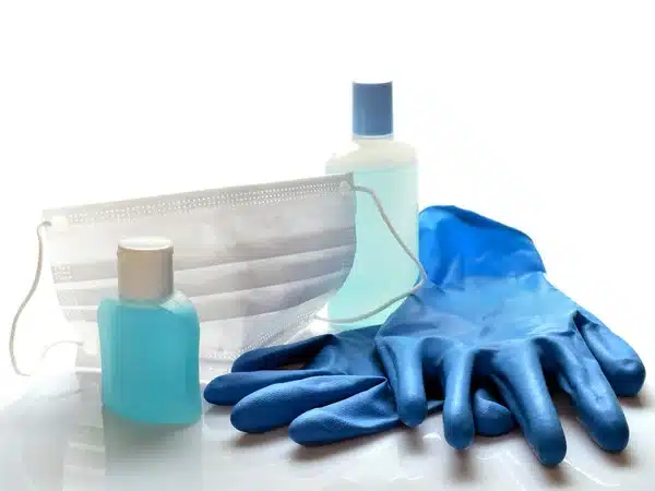PPE Stock Photo A display showcases a disposable face mask, two hand sanitizer bottles, and blue medical gloves on a white background.
