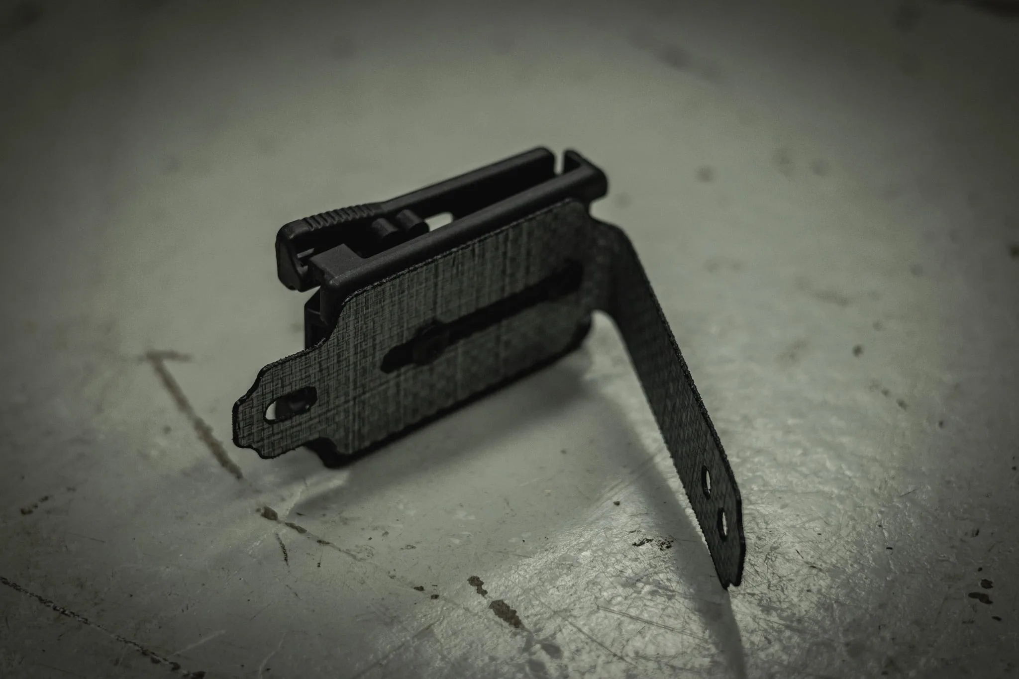 Black L-shaped TEK LOK MOLLE Adapter on grey surface.